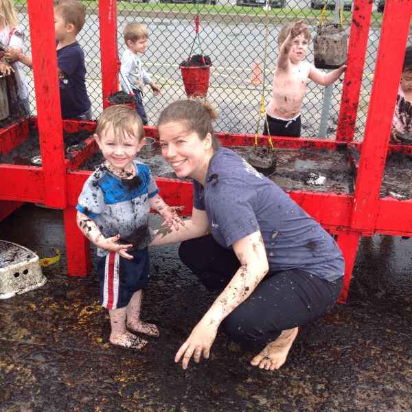 educator and boy posing for a photo infront of a mud kitchen covered in mud